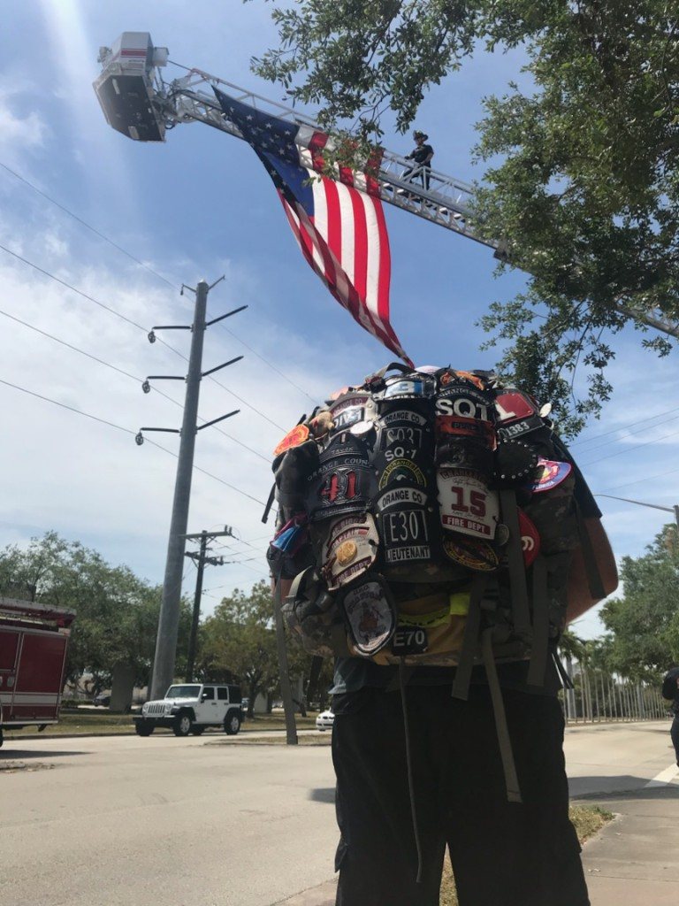 A firefighter seen from behind, with an American flag raised from a ladder truck.